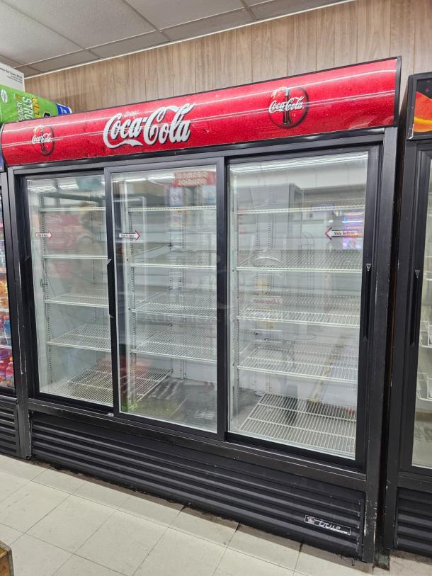 TRUE GDM-69 three glass door merchandiser in working condition, 115V. Features Coca-Cola branding. Visible storage shelves.
