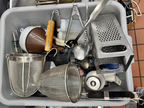 Miscellaneous kitchenware assortment in a bin; includes strainers, grater, funnel, and utensils. Various materials, used condition.