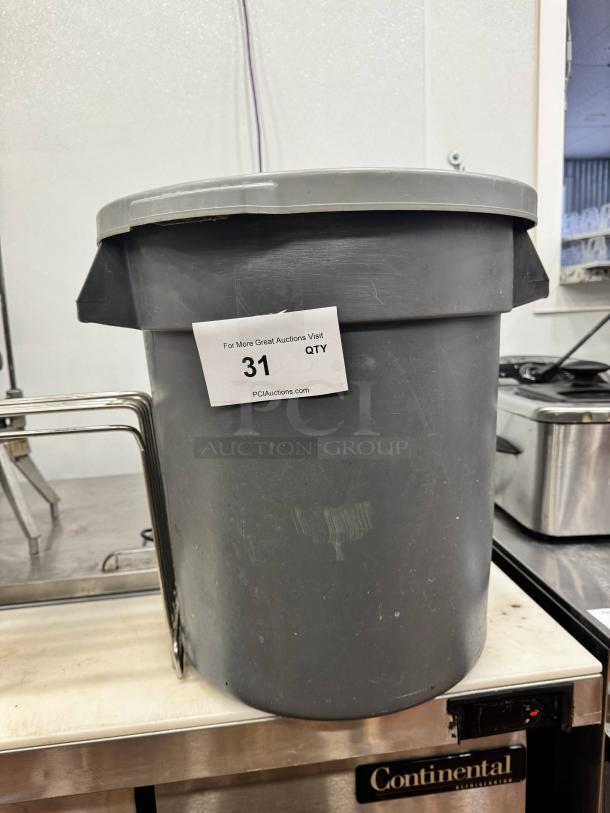 Small gray plastic trash can, cylindrical, no lid. Moderate wear. Label reads "For More Great Auctions Visit 31 QTY PCIAuctions.com."