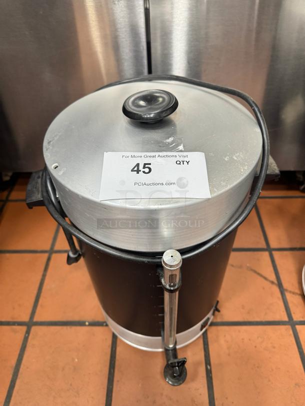 Stainless steel coffee urn with black exterior, top lid, and visible spigot. Item tag reads "45 QTY" from PCI Auctions.