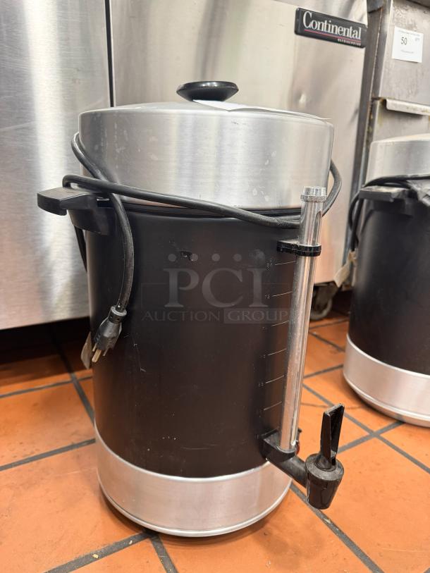 Stainless steel coffee urn with black base, spigot, and power cord, in good condition. No visible brand markings.