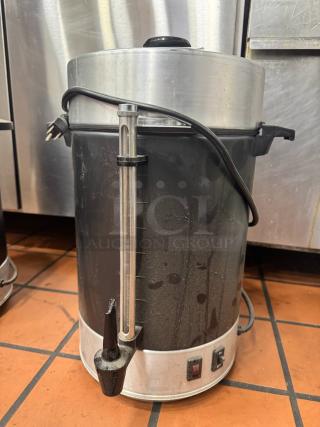 Large coffee urn with spout and gauge, metal and black plastic, used condition, visible power cord and switches.