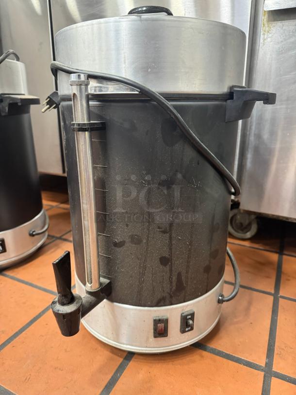 Stainless steel coffee urn with spout, power switch, and capacity gauge. Used condition with visible wear.