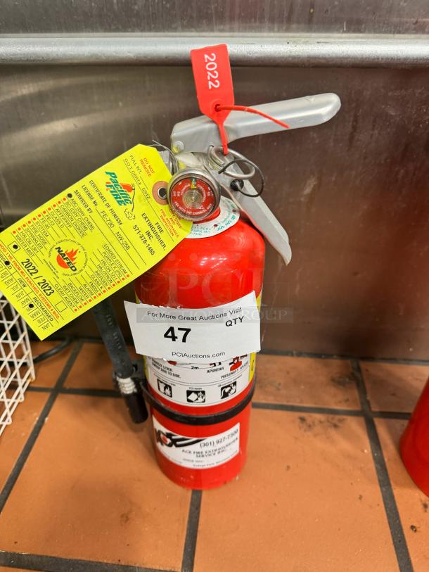 Red fire extinguisher with inspection tag, marked "2022," Pacific Fire Equipment label, gauge showing full charge.