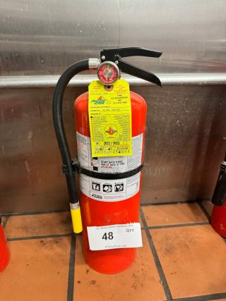 Red fire extinguisher by Pacific Fire with inspection tag dated 2022/2023. Includes pressure gauge and usage instructions.