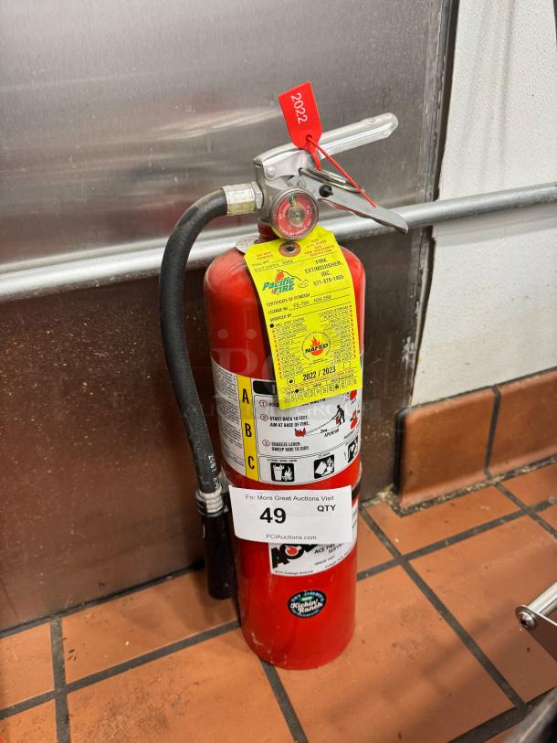 Red fire extinguisher with Pacific Fire label and maintenance tag. Includes instructions label and red tag marked "2022".
