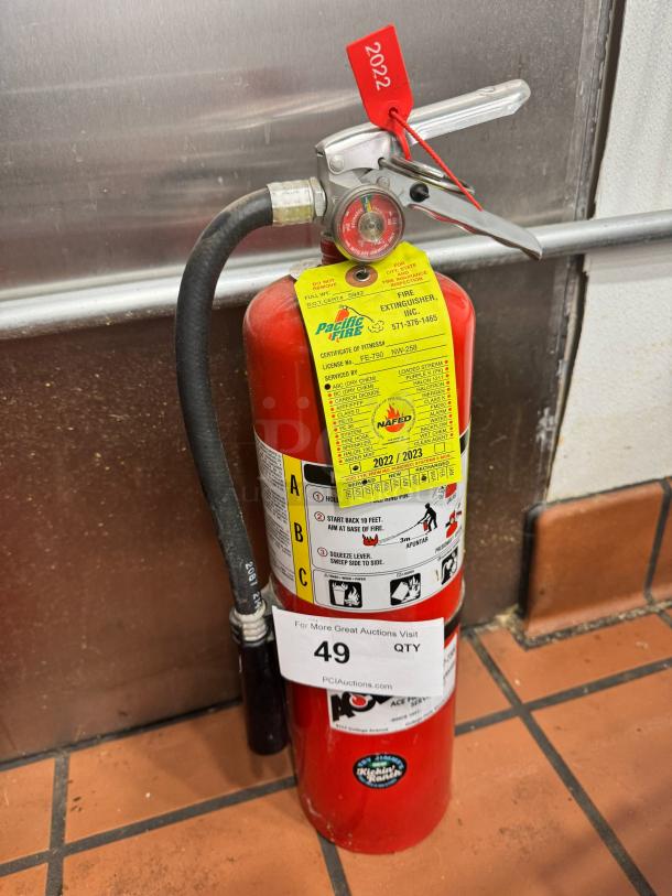Red fire extinguisher with visible instructional labels and a 2022 inspection tag. Features pressure gauge and wall mount.