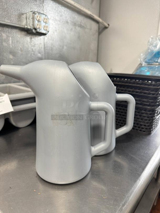 Lot of 2 gray funnel cake batter pouring pitchers with spouts and handles, in good condition, on a metal surface.
