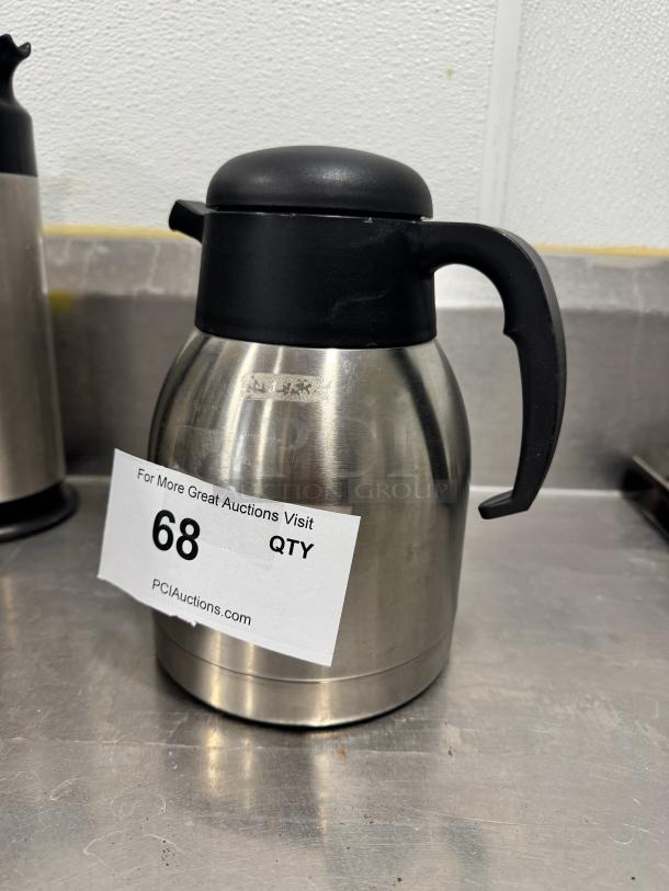 Stainless steel coffee carafe with black lid and handle, show signs of use. Auction label "68 QTY" visible, PCI Auctions.