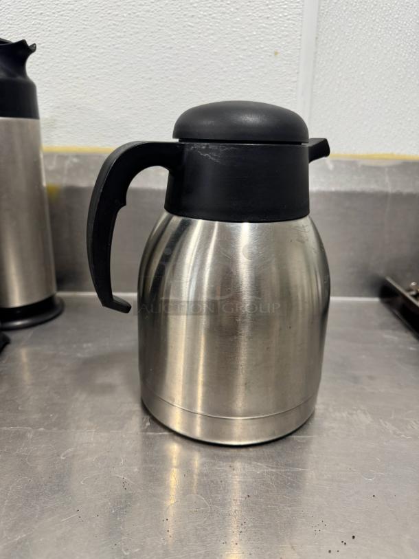 Stainless steel coffee carafe with black lid and handle. Insulated design, in good condition, suitable for hot beverages.