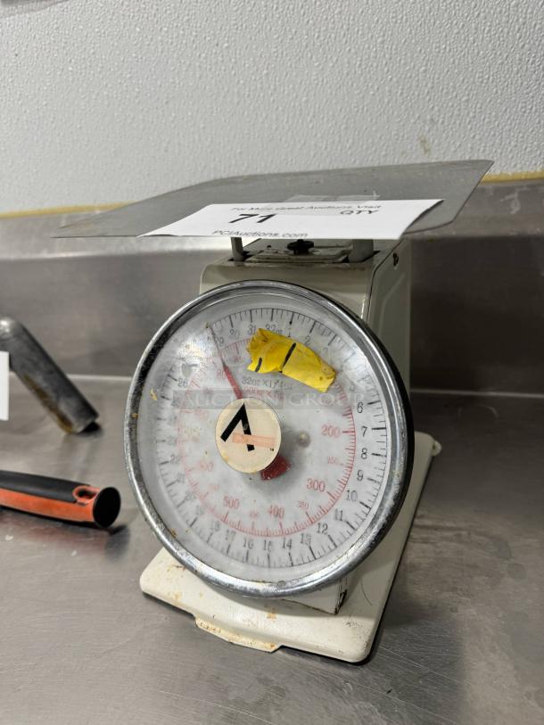 Stainless steel portion control scale, round dial with red and black measurements, used condition, auction tag attached.
