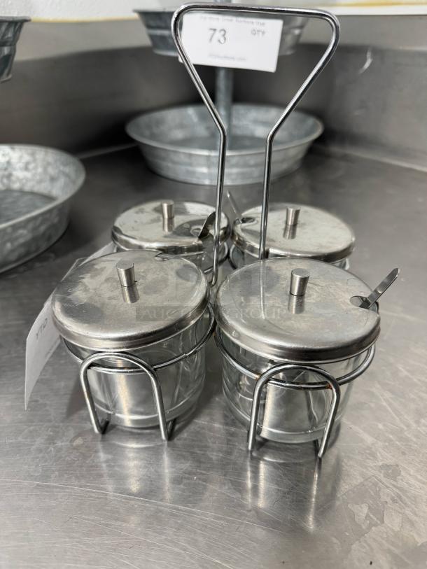 Steel condiment caddy with four glass jars, metal lids, and small spoons, in good condition. Auction lot number 73 visible.