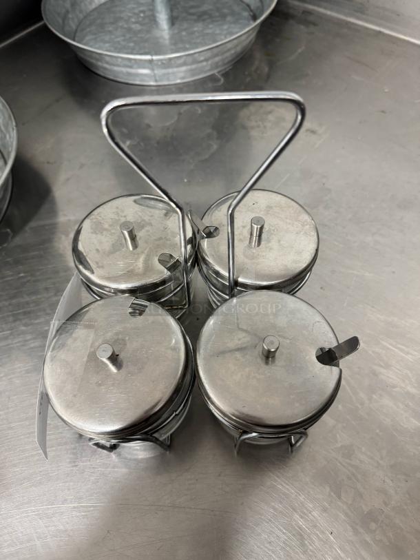 Stainless steel condiment caddy with four jars and handles, ideal for organized serving. Good condition.