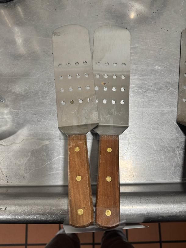 Perforated turner with wood handle, featuring dual stainless steel slotted blades. Handles have brass rivets, good condition.