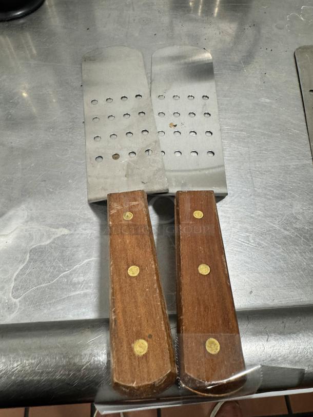Perforated turner with wood handle, stainless steel head, multiple round holes, used condition, visible wear on handle.