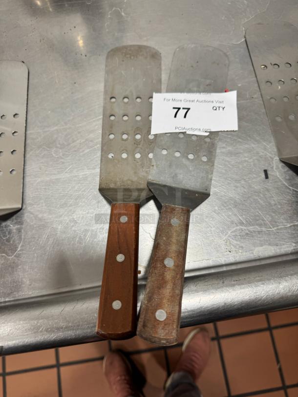 Pair of perforated turners with wood handles; metal blades show wear. Auction tag number 77 visible.