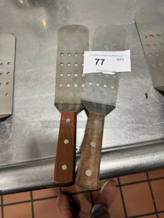 Pair of perforated turners with wood handles; metal blades show wear. Auction tag number 77 visible.