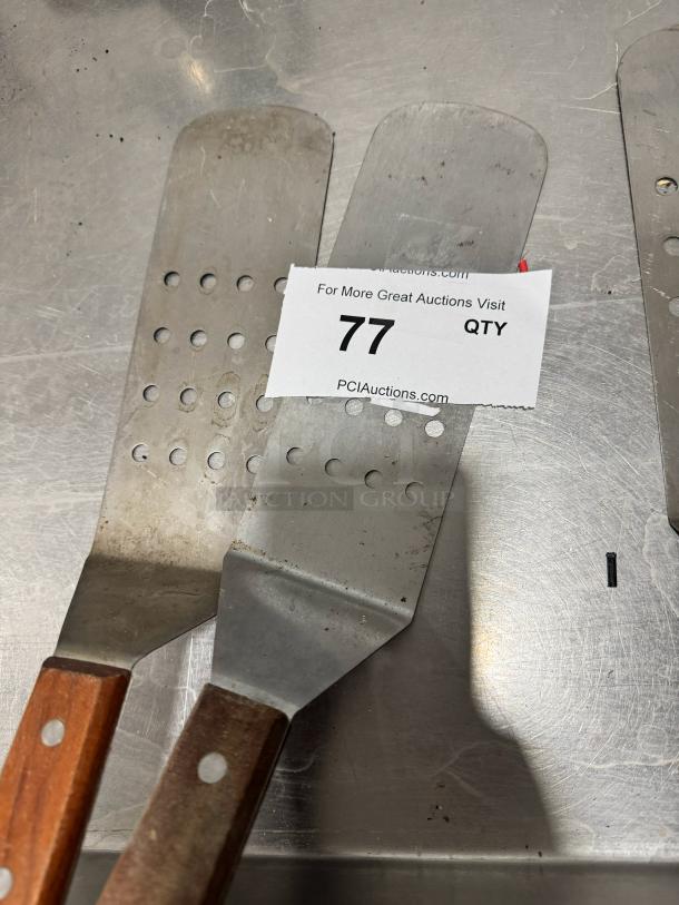Perforated Turner with wood handle, metal blade, slight wear visible. Auction tag reads "77 QTY."