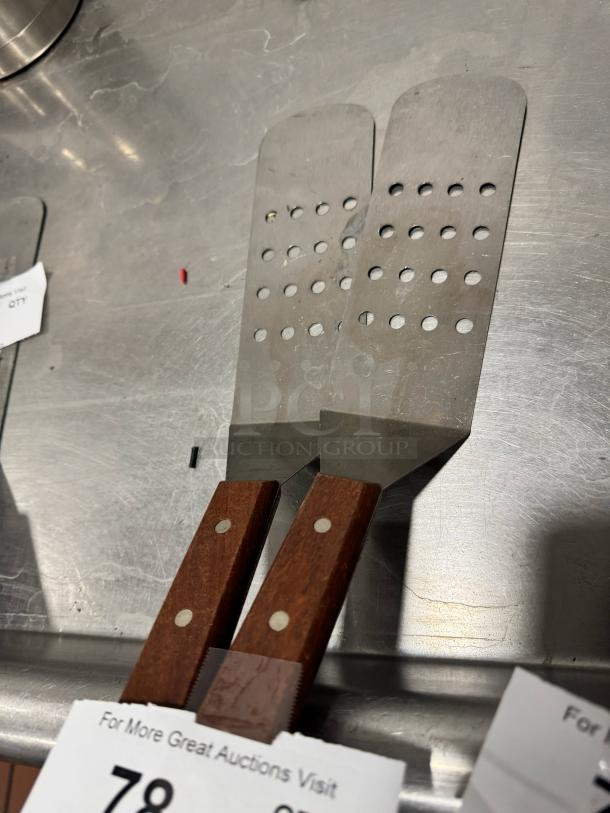 Pair of perforated turners with wood handles, stainless steel blades, riveted design, excellent condition.