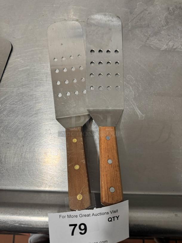 Perforated turner pair with wooden handles, metal blades, in good condition. Auction tag visible with number 79.