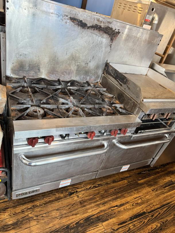 Vulcan 60" commercial gas range with griddle, broiler, and two ovens. Features red knobs, visible wear, sturdy stainless steel.