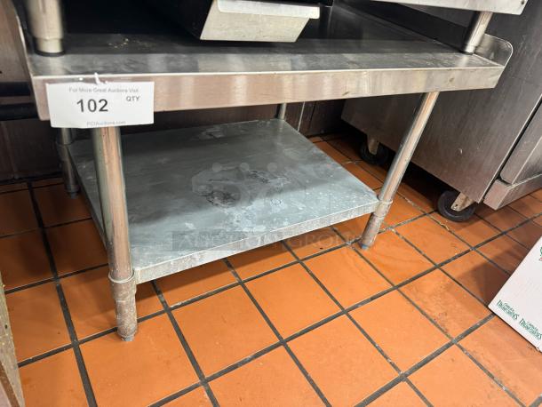36" stainless steel stand with two shelves, visible wear, sturdy legs. Auction lot tag indicates item number 102.