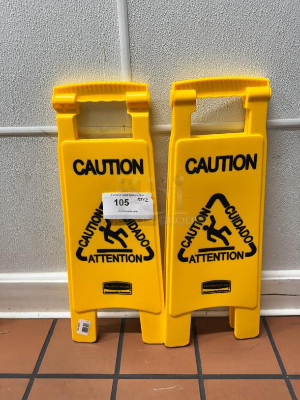 Yellow "Caution" floor signs with bilingual text, featuring slipping symbol. Rubbermaid branding visible at base. Two in set.