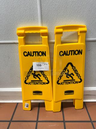 Yellow "Caution" floor signs with bilingual text, featuring slipping symbol. Rubbermaid branding visible at base. Two in set.