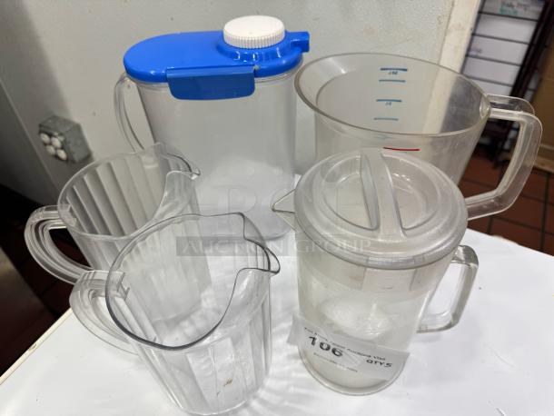 Clear plastic pitcher set, five pieces, various sizes, one with blue lid, measurement markings visible, used condition.