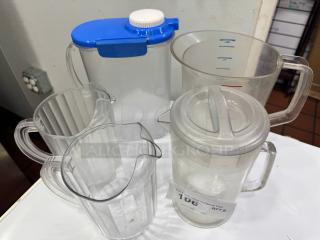 Clear plastic pitcher set, five pieces, various sizes, one with blue lid, measurement markings visible, used condition.