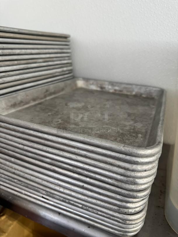 Half-size aluminum baking sheets, model BIDX10, showing signs of wear, stacked vertically on a shelf.