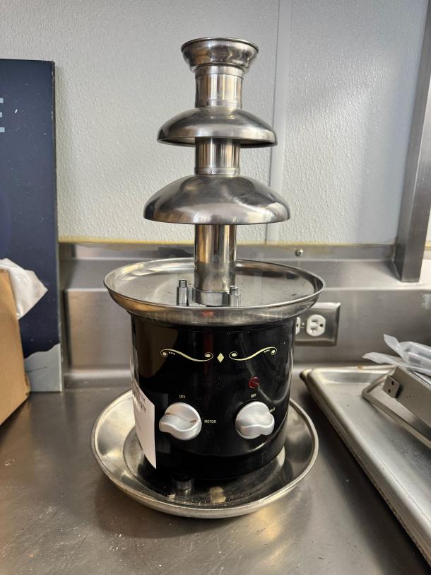 Brand new chocolate fondue fountain with stainless steel tiers and black base. Features control knobs for heat and motor.