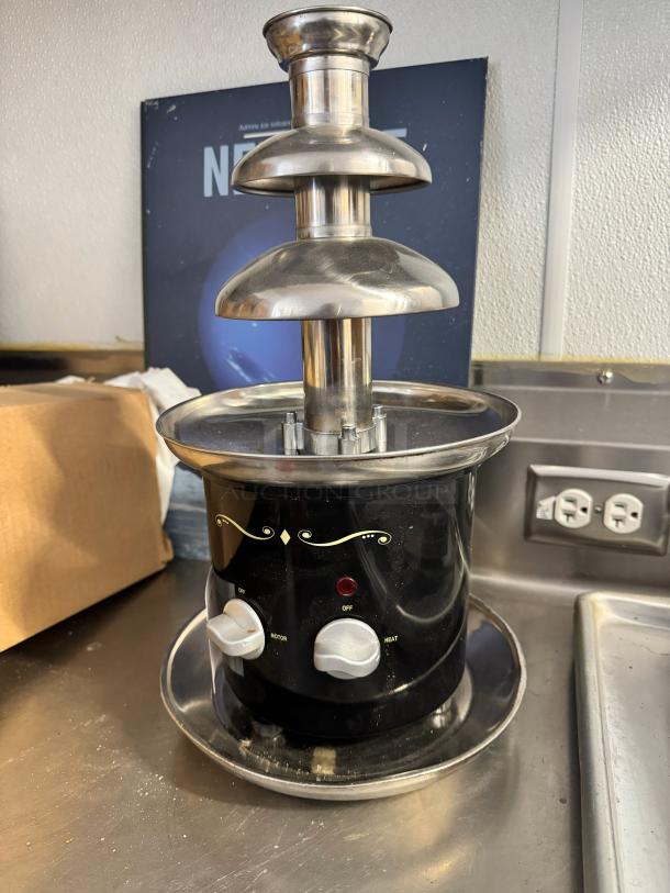Brand new chocolate fondue fountain with stainless steel tiers, black base, and heating/motor controls.