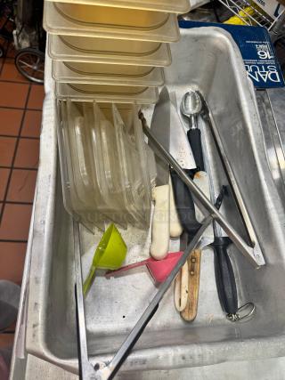 Assorted kitchenware in tray, including plastic containers, measuring cups, and utensils. Mixed condition.