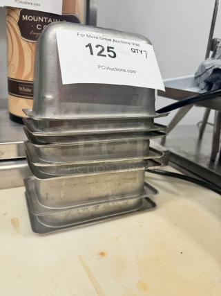 Stainless steel food pan BIDX7, set of seven, used condition, stacked with auction tag "125 QTY 7" visible, showing minor wear.