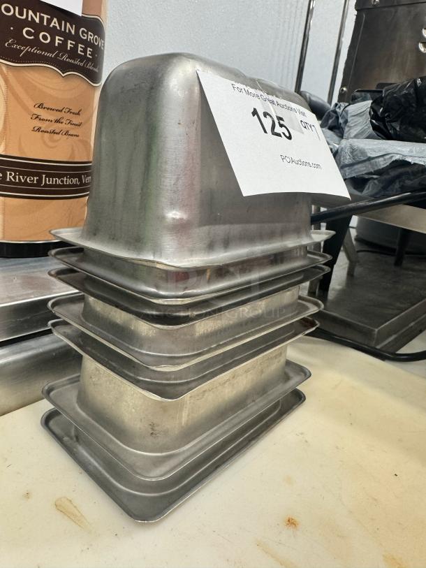 Stack of stainless steel food pans, model BIDX7, in used condition. Auction label reads "125 QTY1."
