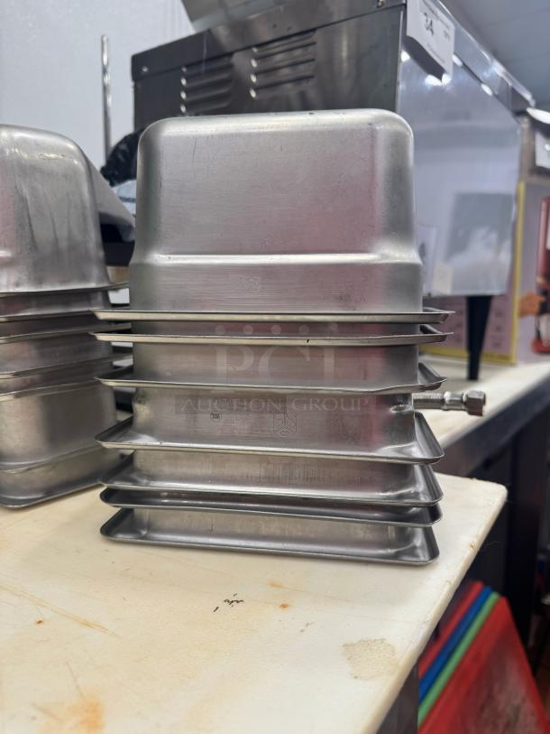 Stacked stainless steel food pans, model BIDX7, with visible manufacturer markings, in good condition.