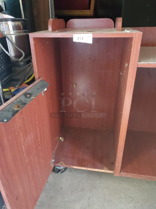 Wood top tray receptacle with open door, wood grain finish, and wheels. Shows wear and item tag labeled "111 QTY."