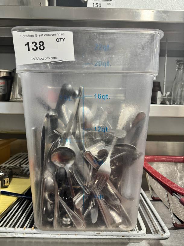 Bulk stainless steel cutlery in a 22-quart container; includes spoons, forks, and knives; auction label "138" visible.