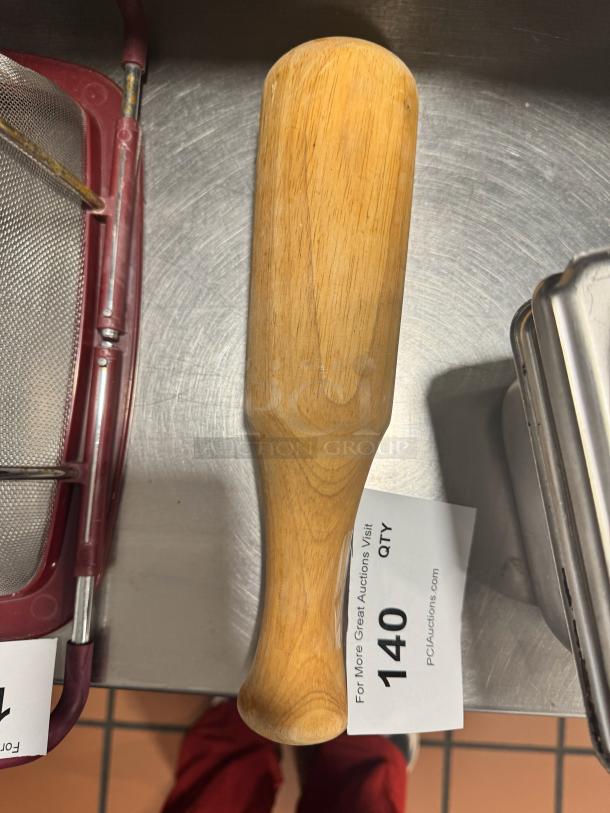 Wood muddler with smooth finish, natural grain, and ergonomic handle. Auction tag reads "140 QTY, PCIAuctions.com".