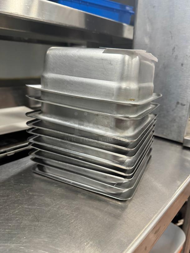 Stainless steel food pans, model BIDX10, stacked; durable, used, minor surface wear, ideal for commercial use.