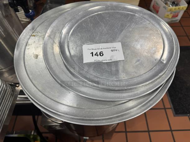 Lot of 4 metal pizza pans with visible wear, auction label with lot number 146, displayed in a kitchen setting.