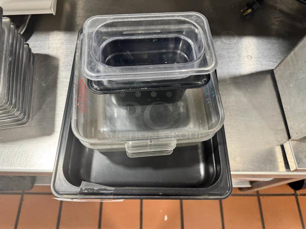 Lot of 6 plastic food pans stacked; clear and black; varying sizes; condition appears used; commercial kitchen setting.