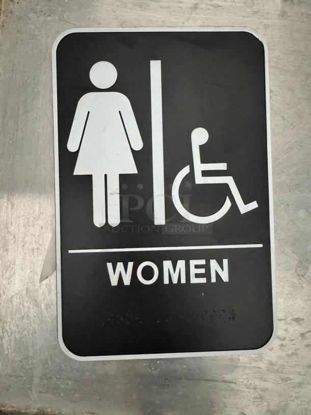 Black and white women's restroom sign with wheelchair access symbol. Features braille and text, made of durable plastic.