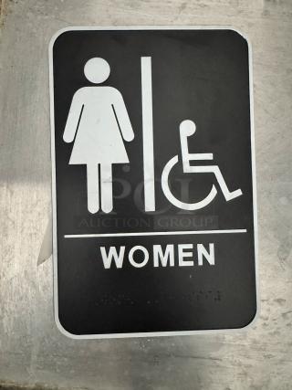 Black and white women's restroom sign with wheelchair access symbol. Features braille and text, made of durable plastic.