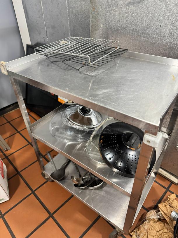 Stainless Steel utility cart with three shelves, wheels, used condition, includes wire rack and cooking utensils on shelves.