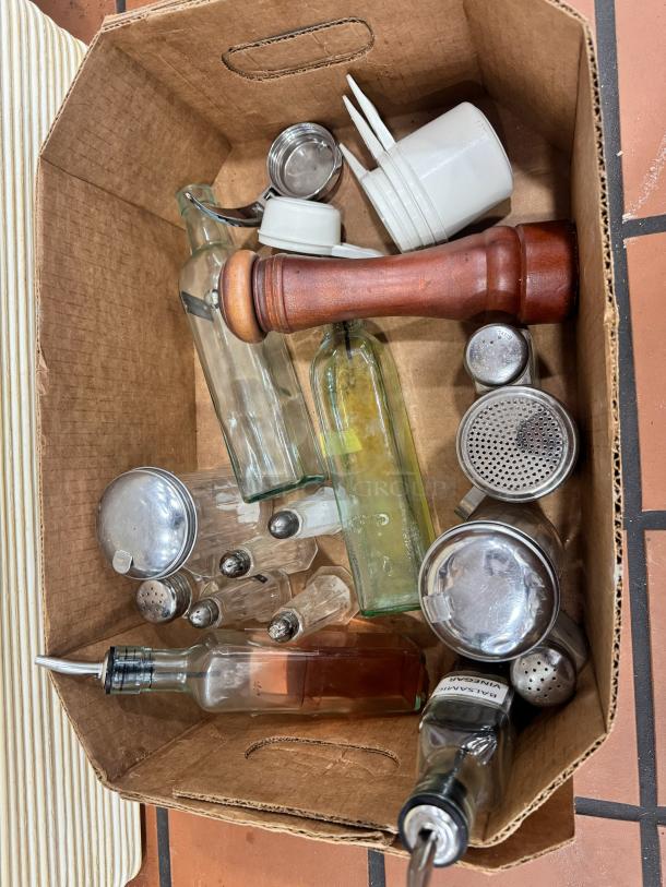 Box of miscellaneous kitchenware including glass bottles, wooden grinder, salt and pepper shakers, metal scoops, and white ceramic cups.