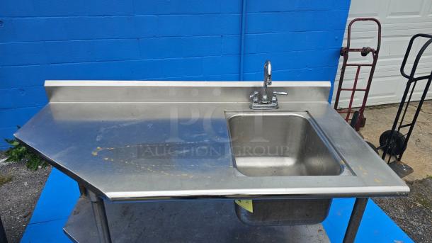 Stainless steel work table with integrated sink. Needs faucet repair. Visible wear on surface. Ideal for commercial use.
