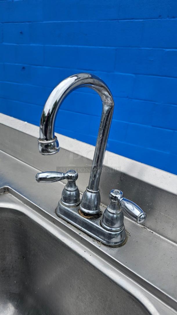 Stainless steel work table with integrated sink; faucet needs repair; durable surface; ideal for commercial use.