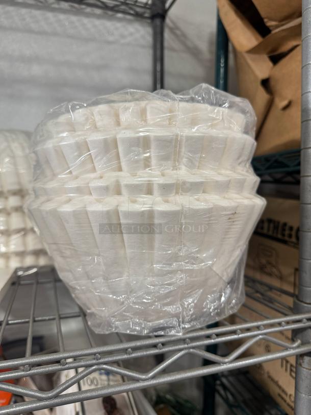 Stack of white coffee filters wrapped in clear plastic, resting on a metal shelf. Suitable for drip coffee makers.